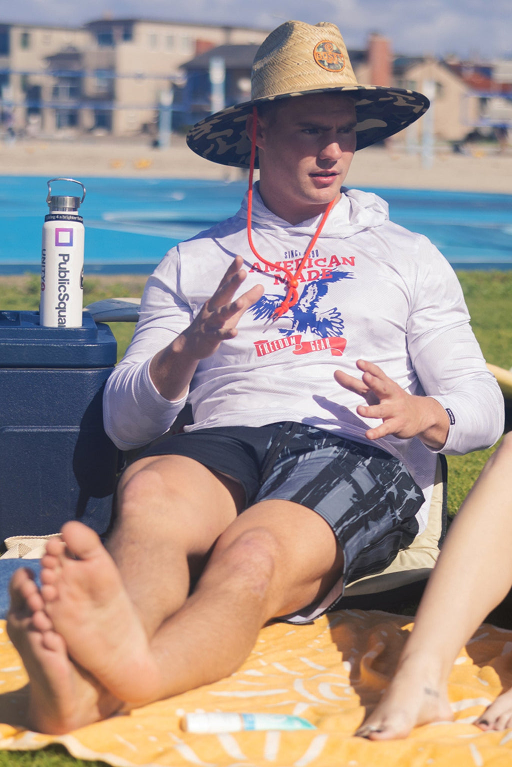 Man sitting outside wearing a WSI White Long Sleeve hoodie with a patriotic American Made Print and WSI Board shorts