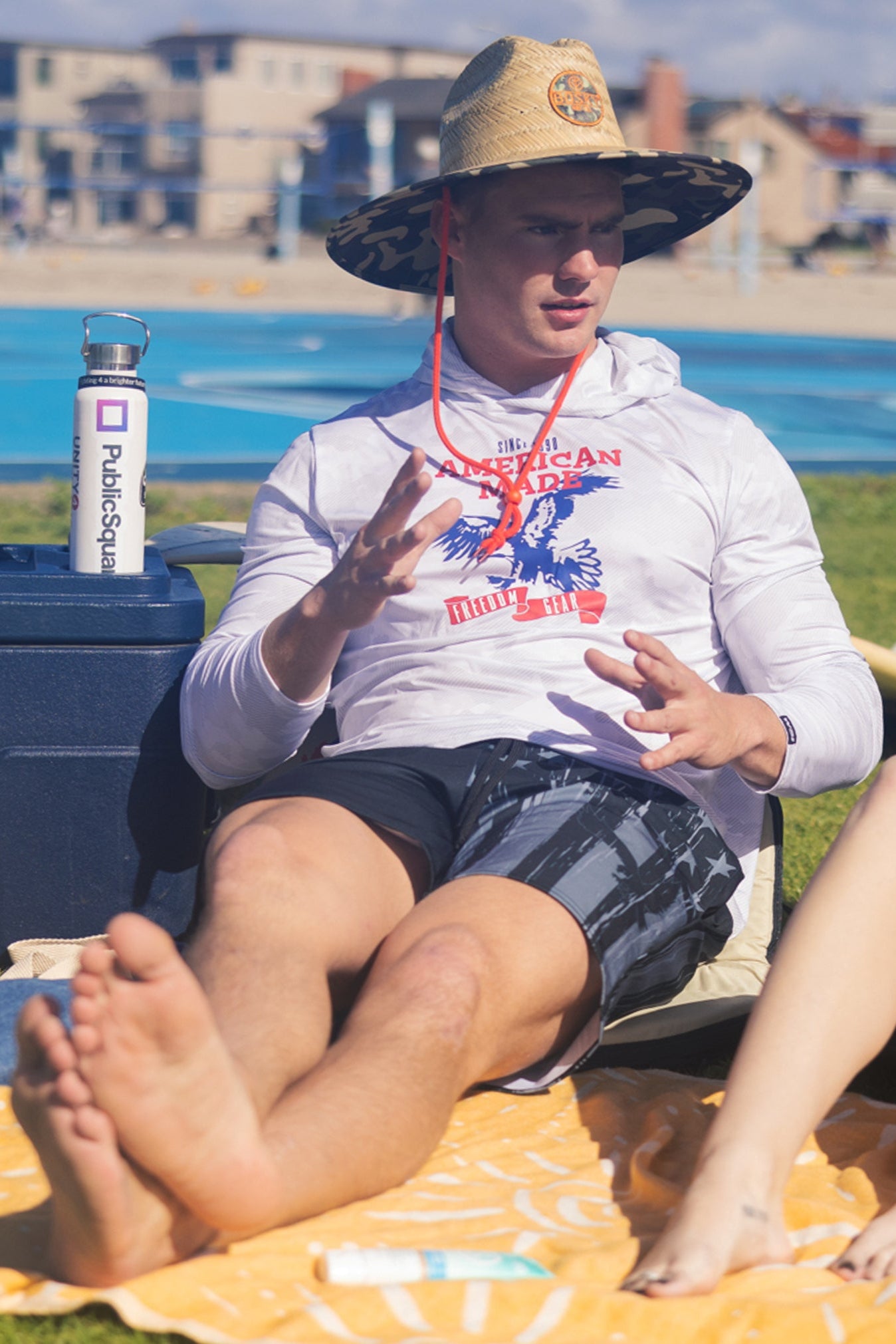 Man sitting outside wearing a WSI White Long Sleeve hoodie with a patriotic American Made Print and WSI Board shorts