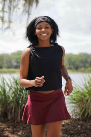 Woman in black top and maroon skirt standing outdoors with trees and water in the background