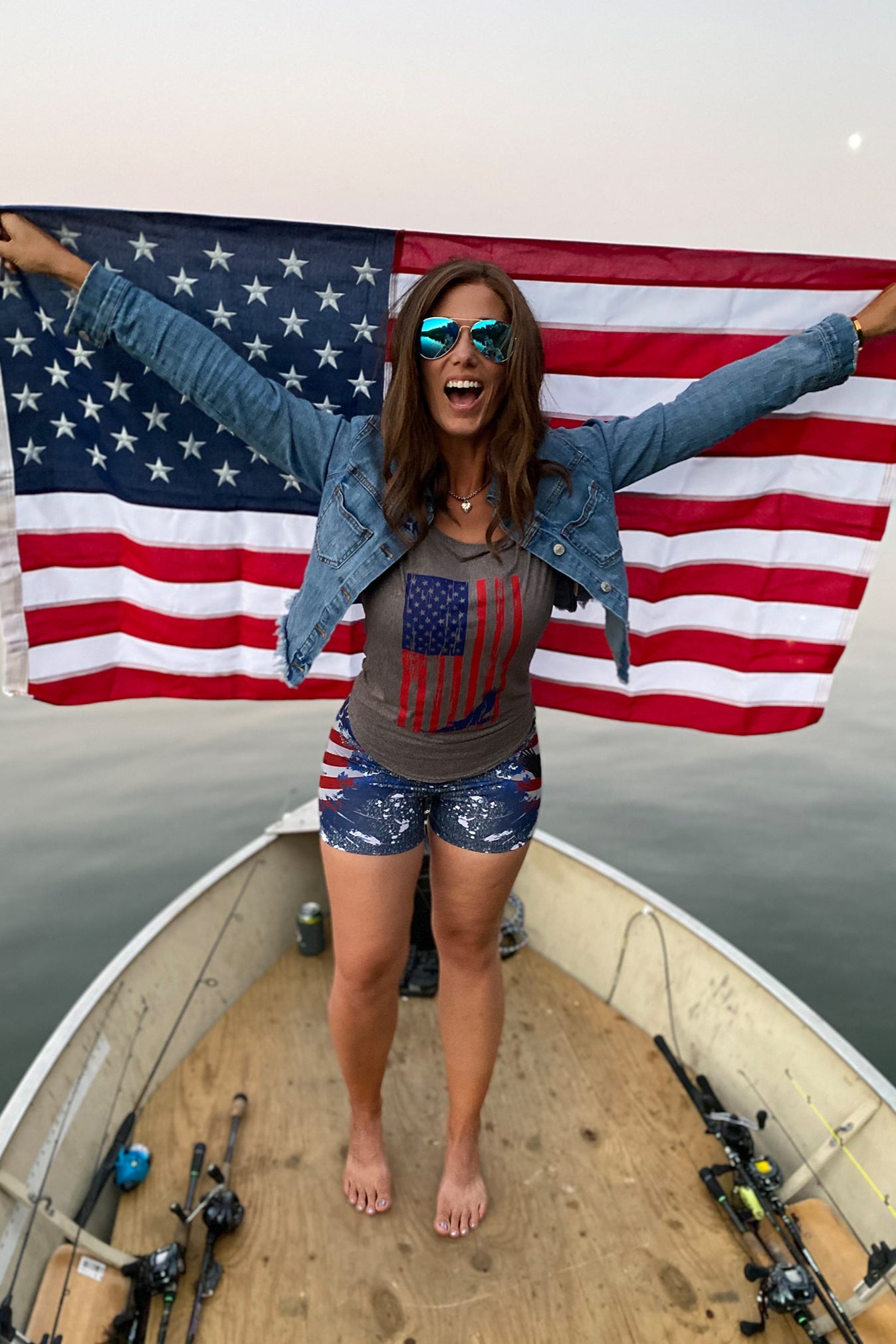 Women standing on a boat holding an American Flag and Wearing WSI Patriotic Shirt and Spandex Shorts