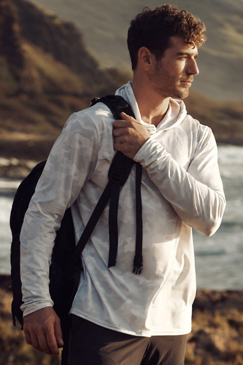 Man wearing a back pack and WSI Sports Performance Mesh whiteout camo lightweight hoodie while out hiking in mountains